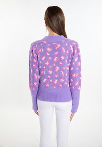 Maglione viola soffice con stampa leopardata rosa e bianca, con maniche lunghe e orlo a coste. Indossato con pantaloni bianchi.