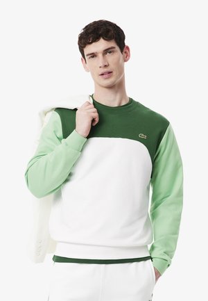 Sweat-shirt coloré en blocs vert et blanc avec un col rond et des poignets côtelés. Présente le logo Lacoste sur la poitrine et une texture lisse.