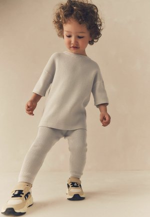 Ljusgrått ribbat tvådelat set för barn, med en lös topp och tajta byxor, parat med beige och svarta sportskor.