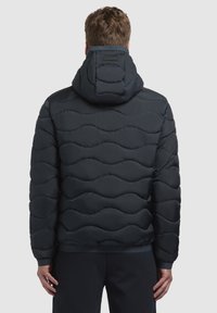 Donkerblauwe pufferjas met een gewatteerd golfpatroon, capuchon en elastische manchetten. Glad textuur en zachte voering, geschikt voor koude weersomstandigheden.