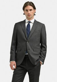 Mörkgrå skräddarsydd kostym med notch-lapel, en knappslutning och två framfickor. Vit skjorta och mörkblå slips. Slät tygtextur.