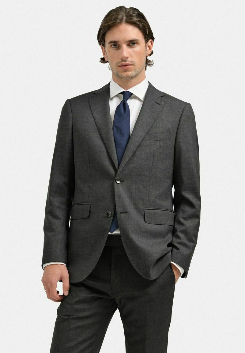 Mörkgrå skräddarsydd kostym med notch-lapel, en knappslutning och två framfickor. Vit skjorta och mörkblå slips. Slät tygtextur.