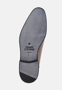 Bruine leren schoenzool met een gladde grijze afwerking, voorzien van een gegoten logo, maat 8, en metalen studs langs de rand.