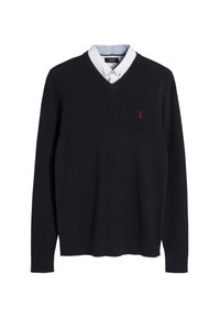 Laivastonsininen neulepaita V-kauluksella, jonka alla valkoinen kauluspaita ja rinnan kohdalla punainen kirjailtu logo.