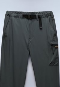 Šedé venkovní kalhoty s elastickým pasem, nastavitelným pásem, předními kapsami a boční kapsou na zip. Hladká, lehká tkanina.
