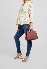 Floral print blouse with three-quarter sleeves; blue denim jeans; maroon handbag with tan handles; white strappy sandals with block heels.