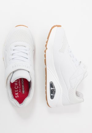 Baskets blanches Skechers avec un dessus perforé, sangle réglable et une semelle en caoutchouc beige avec un rembourrage d'air visible. Semelle intérieure rouge rembourrée.