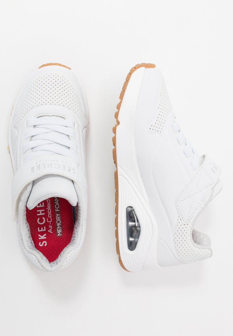 Witte Skechers sneakers met een geperforeerde bovenkant, verstelbare band en een tan kleurige rubberen zool met zichtbare luchtkussen. Rode gevoerde binnenzool.