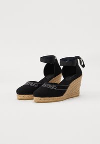 Juodos kanvos espadrilės ant platformos su apvaliu priekiu, kulkšnies dirželiais, jute apvyniotomis platformomis ir "Valentino" logotipu priekyje.