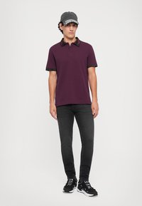 Camisola polo bordeaux com colarinho e mangas padronizados, combinada com jeans slim-fit pretos e ténis pretos com detalhes brancos.