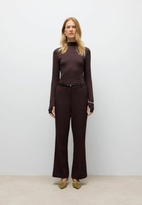 Maglione a collo alto aderente bordeaux e pantaloni a gamba larga, entrambi in un tessuto liscio. Accentuato con una cintura nera e scarpe beige con punta.