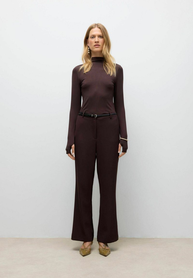 Maglione a collo alto aderente bordeaux e pantaloni a gamba larga, entrambi in un tessuto liscio. Accentuato con una cintura nera e scarpe beige con punta.