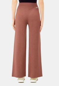 Pantaloni a gamba larga color rosa polveroso, realizzati in un tessuto morbido. Presentano una vita alta con un discreto marchio vicino alla parte posteriore.
