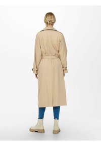 Beige trenchcoat med belte i midjen, lange ermer og en lett glans. Har justerbare stropper ved ermene og en klassisk krage.