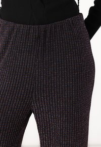 Black high-waisted pants with vertical multicolored stripes. Textured fabric features subtle shimmer, enhancing the overall pattern and depth.