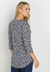 Top blu navy con stampa animale bianca, maniche a tre quarti, scollo rotondo e design con orlo curvato; realizzato in tessuto morbido e testurizzato.
