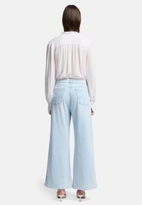 Jeans azzurri a gamba larga, in vita alta, con un semplice design delle tasche posteriori. Abbinati a una camicetta bianca e tacchi beige, presentano una superficie liscia.