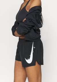 Pantalones cortos deportivos negros con un logo de Nike blanco, fabricados con un tejido ligero, cinturilla elástica y aberturas laterales para facilitar el movimiento.