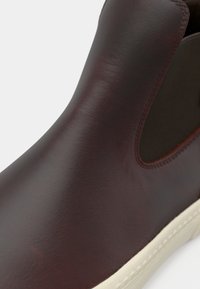 Hnědé kožené kotníkové boty s elastickými bočními panely, elegantní design, texturovaný povrch a krémová gumová podešev. Bez viditelných vzorů nebo kovových prvků.