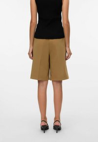 Bruine op maat gemaakte shorts van een gladde stof, met een losse pasvorm en zijnaad, gecombineerd met zwarte enkelbandjeshakken en een zwarte top.