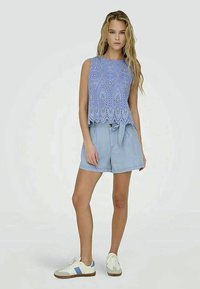 Vaaleansininen pitsipaita, jossa on aaltoileva helma, yhdistettynä vaaleansinisiin shortseihin ja valkoisiin kenkiin, joissa on sinisiä yksityiskohtia. Sujuvat tekstuurit, rento istuvuus.