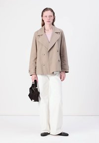 Beige dvouřadový blejzr s velkými klopami, nošený přes světle růžový top. V páru s bílými širokými kalhotami a držící černou kabelku.