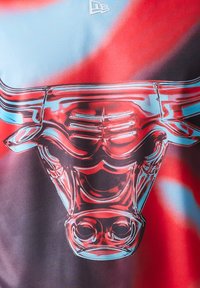 Κόκκινη και μπλε γραφική μπλούζα με εμφανές, διαφανές λογότυπο ταύρου, με περίπλοκες λεπτομέρειες και απαλή υφή.