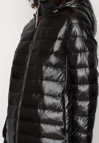 Czarna kurtka puchowa o błyszczącej powierzchni, z poziomym pikowaniem, zamek błyskawiczny i przymocowany kaptur. Posiada różowe sznurki do regulacji oraz logo.