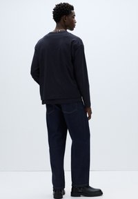 Temno modra srajca z dolgimi rokavi in sproščenim pristopom, kombinirana s temno modrimi kavbojkami in črnimi usnjenimi škornji. Ima okrogel izrez in minimalne detajle.