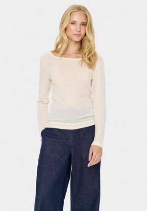Long-sleeve cream shirt with a wide neckline and soft texture, paired with dark blue wide-leg trousers featuring patch pockets.