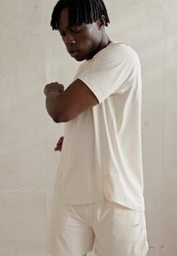 Camisa atlética de un beige claro y pantalones cortos de tela suave y elástica. Diseño simple con mangas cortas y un sutil logo en los pantalones cortos.
