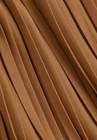 Gros plan d'un tissu marron plissé avec une texture fine et des plis verticaux espacés uniformément.