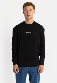 Black sweatshirt made of cotton, featuring a crew neckline and long sleeves. Centered white text reads "DENIM PROJECT." Casual fit.