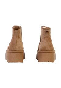 Botines hasta el tobillo de ante color canela con acabado texturizado, puntera redonda y suela con plataforma. Presentan una lengüeta en el talón y detalles de costuras laterales.