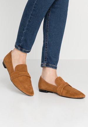 Suède loafers in tan met een gevouwen banddetail, puntige neus en lage zwarte hak. Gecombineerd met donkerblauwe slim-fit jeans.