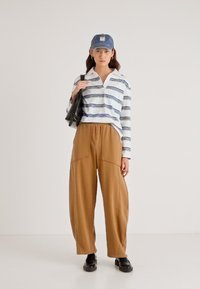 Gestreept shirt met lange mouwen en kraag, bruine broek met wijde pijpen en een denim pet. Zwarte handtas en stevige zwarte schoenen maken de outfit compleet.