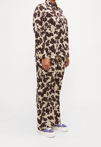 Blusa a pois marrone e crema con pantaloni coordinati, caratterizzata da un colletto e maniche lunghe, abbinata a scarpe con dettagli viola.