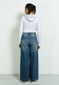 Biała, krótka bluza z kapturem z tyłu, zestawiona z dżinsami w kolorze blądym niebieskim o wysokim stanie i szerokich nogawkach, posiadającymi dwie tylne kieszenie.