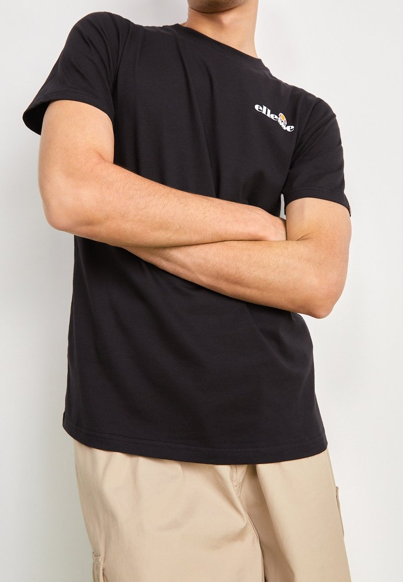 T-shirt en coton noir à manches courtes, col rond, avec un petit logo blanc sur la poitrine. Accompagné de shorts cargo beiges.