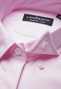 Jasnoróżowa koszula z teksturowanej tkaniny, z wywijanym kołnierzykiem i pojedynczym białym zapięciem na guzik. Metka głosi "LANCERTO COMFORT PLUS."