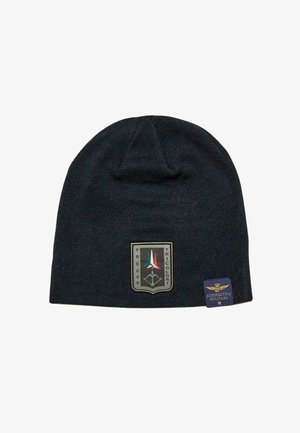 Berretto di maglia nero con una toppa raffigurante un design a scudo. Include strisce verticali colorate e un'etichetta secondaria con un emblema dell'aviazione.
