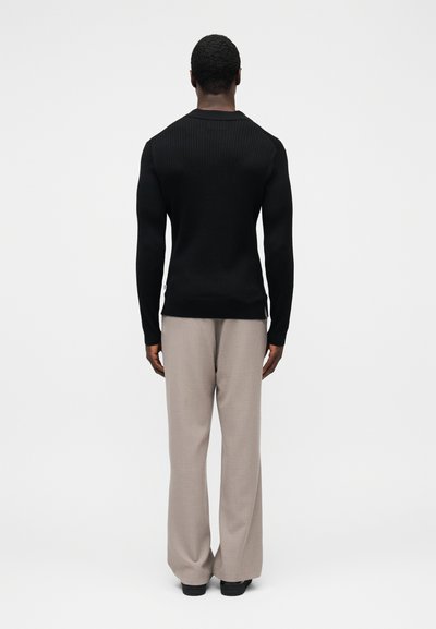 Pull noir à manches longues côtelé avec un col rond, porté avec un pantalon beige à jambes larges, vu de dos.