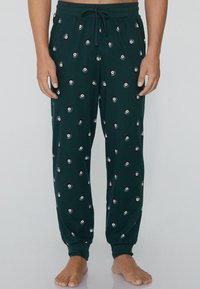 Groene pyjamabroek van zacht materiaal, met een patroon van kleine witte stippen met zwarte middens. Elastische tailleband met trekkoord.