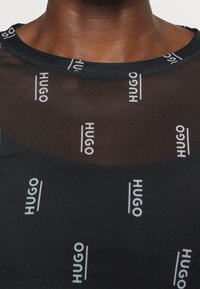 Schwarzes Mesh-Top mit sich wiederholendem weißen "HUGO"-Logo, Rundhalsausschnitt und glatter Textur, mit insgesamt taillierter Passform.