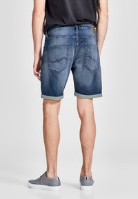 Džínové šortky v tmavě modré barvě s vybledlým efektem. Ohnuté manžety a dvě zadní kapsy s nenápadným prošíváním. Nosené s šedými teniskami.