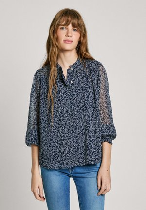 Marinblommig blus med genomskinliga ärmar, volangkrage och knappdetaljer. Har lättviktigt material och en lös passform, i kombination med blå jeans.
