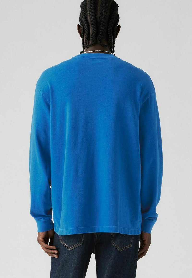 Camisa de algodón azul de manga larga con un corte estándar, que presenta un cuello redondo y un dobladillo recto. Textura suave, sin patrones ni gráficos.