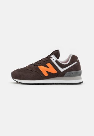 Mørkebrun New Balance sneaker med lys orange "N" logo, hvid og grå mellemsål og sort slidbane vist fra ydersiden.