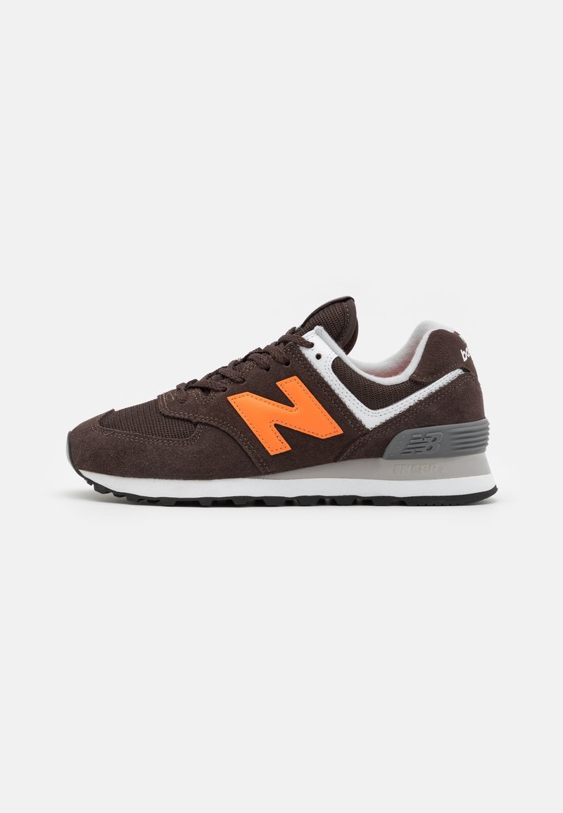 Baskets New Balance marron foncé avec logo "N" orange vif, semelle intermédiaire blanche et grise, et semelle extérieure noire vues de côté.