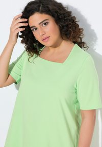 Top verde chiaro con maniche corte e scollo quadrato. Realizzato in tessuto morbido, presenta una vestibilità ampia e cuciture minime per il comfort.
